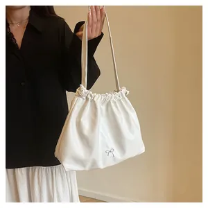 Detail of white pleated tote bag featuring a silver metal bow and soft PU leather texture