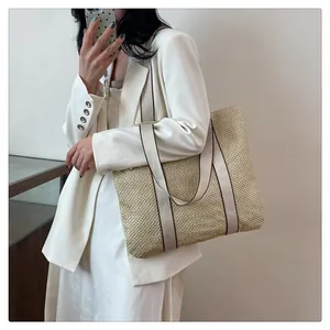 Close-up of a woven straw tote bag with thick beige and brown handles worn by a model