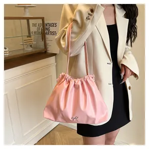 Pink pleated cloud tote bag with silver metal bow detail worn as an underarm shoulder bag