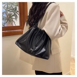Detailed view of black pleated tote bag with silver bow charm and drawstring detail