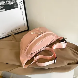 Detail view of pink satin fanny pack with dual zippers on a khaki blazer background