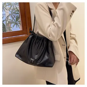 Detail of black pleated drawstring tote bag with a silver bow ornament on beige blazer