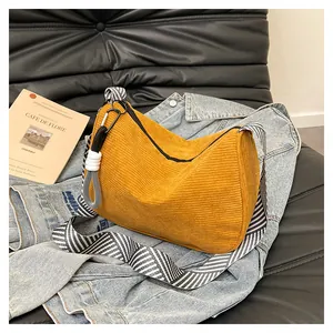 Detail of yellow corduroy crescent bag with woven knot and striped strap on denim