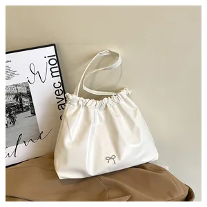 Close-up of white ruched shoulder bag featuring a silver metal bow charm and drawstring