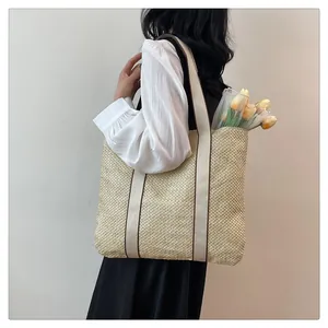 Detail of woven straw tote bag featuring creamy white handles and a casual beach design