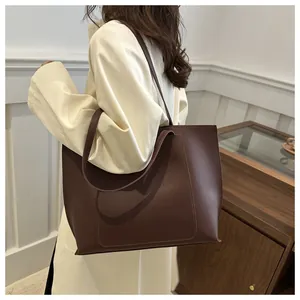 Détail d'un sac cabas en cuir marron avec surpiqûres en U porté par un mannequin en manteau beige