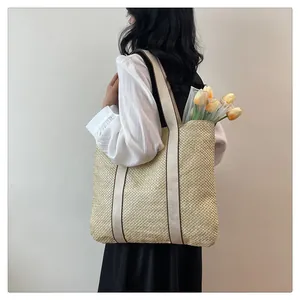 Outdoor shot of a woven straw tote bag with cream shoulder straps and brown stripe detail
