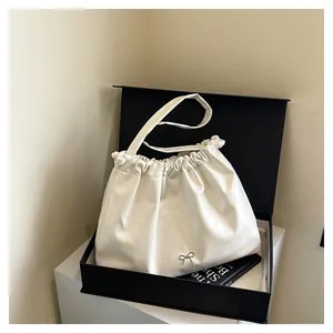 Detail of white pleated shoulder bag with silver bow accent in a premium gift box