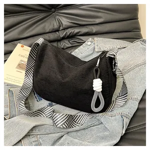 Detail of black corduroy hobo bag texture with a striped shoulder strap on denim fabric