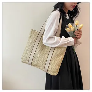 Asian model showcasing a large woven straw tote bag with cream-colored ribbon straps