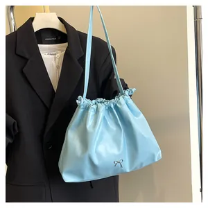 Close-up of light blue pleated hobo bag featuring a silver metal bow and slim shoulder strap