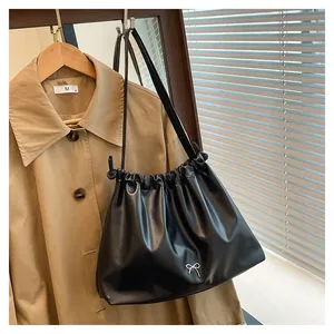 Detailed close-up of a pleated black tote bag featuring a small silver bow metal buckle