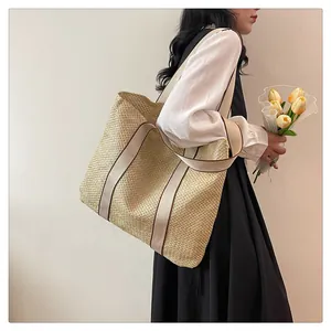 Detail of a large woven straw tote bag with wide canvas straps held by a model