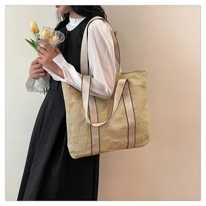 Detail of a large straw tote bag with wide fabric shoulder straps on a female model