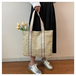 Close-up of a large straw tote bag with beige woven texture and brown ribbon handles