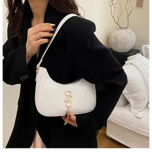 Détail du sac croissant blanc avec logo S doré et gland métallique sur un blazer