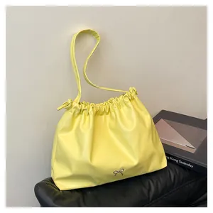 Detail view of yellow ruched tote bag with silver bow accent on a stylish pedestal
