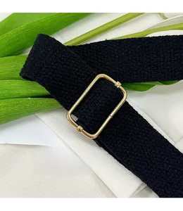 Gros plan de la bandoulière noire tissée avec boucle dorée sur fond décoratif