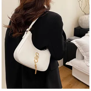 Sac bandoulière beige en forme de croissant avec pompon doré porté par un mannequin chic