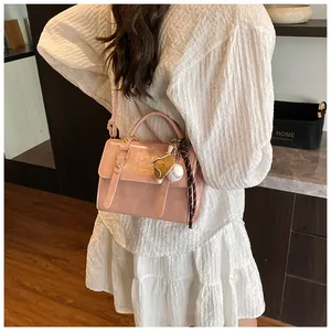 Detail of pink PU leather handbag with fashion logo and baseball bear pendant on model