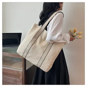 Detailed side view of a large beige woven tote bag worn on a woman's shoulder