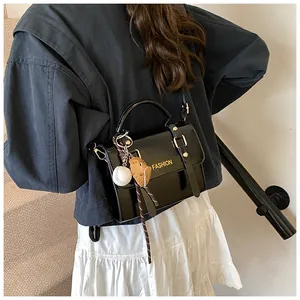 Detail of glossy black satchel with metal buckle and baseball glove charm on model