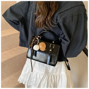 Detail of black glossy handbag with gold V ornament and creative baseball charm accessory