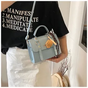 Detail of light blue PU leather handbag with gold buckle and bear charm accessory