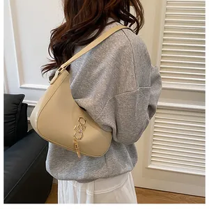 Détail du sac hobo en croissant beige avec breloque logo en métal doré sur un modèle