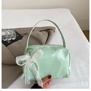 Detail of mint green shoulder bag with pearl lace bow charm on white fabric background