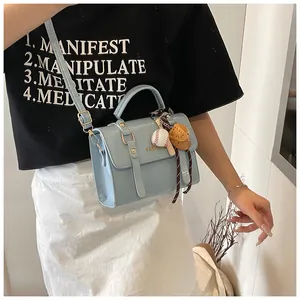 Detail of light blue glossy leather handbag featuring baseball theme charms and crossbody strap