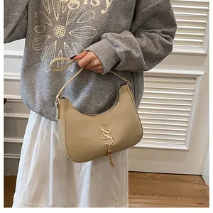 Détail du sac sous l'aisselle beige en demi-lune avec logo doré et pompon décoratif