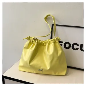 Detail of a bright yellow pleated shoulder bag featuring a silver metal bow accent
