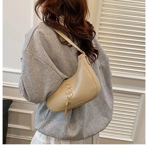 Détail du sac demi-lune beige avec logo S doré et gland métallique sur un mannequin