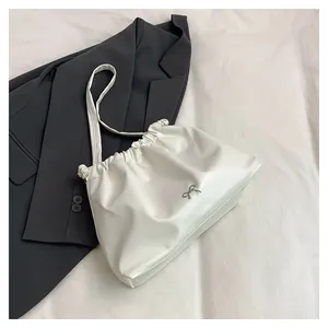 Detail of cream pleated tote bag with silver bow accent on a stylish grey suit jacket