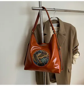 Detail of caramel leather hobo bag with ethnic elephant embroidery hanging on a metal rack