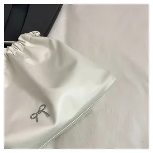 Detailed macro view of white drawstring tote bag with a metallic silver bow logo