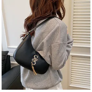 Détail d'un sac hobo noir avec ferrures dorées et pompons porté par un mannequin en intérieur