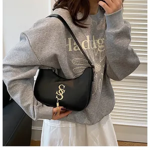 Détail d'un sac demi-lune noir avec logo S doré et gland porté par un mannequin