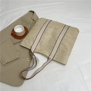 Minimalist beige woven straw tote bag with canvas straps on a stylish white fabric background