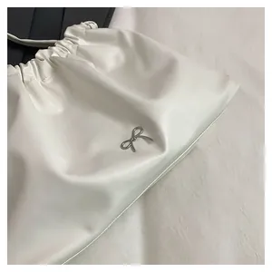 Detail of white pleated handbag featuring a silver metal bow charm and soft PU leather