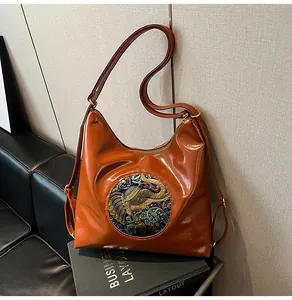 Detail of caramel brown bag with ethnic elephant metal emblem and glossy leather finish