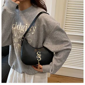 Détail du sac croissant noir avec logo double S doré et pendentif à pompon métallique