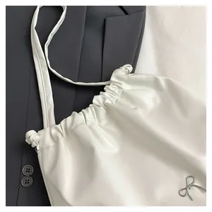 Close-up of white drawstring shoulder bag featuring a delicate silver metal bow detail