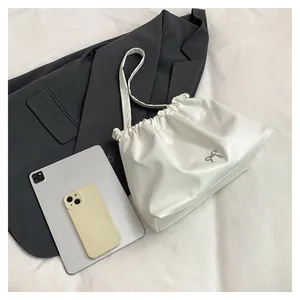 Detail of white pleated tote bag with silver bow accent and drawstring on a grey blazer