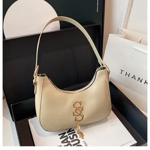 Détail du sac croissant beige avec logo doré et pompon sur magazine de mode