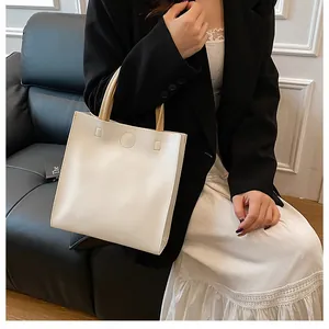Detail of minimalist cream tote bag with brown handles on a gray sofa in office setting