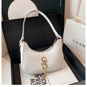 Détail d'un sac demi-lune blanc avec boucle dorée en S et pendentif à chaînette