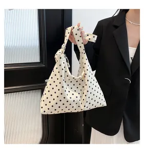 Dettaglio di una borsa tote in tela a pois bianchi e neri portata da una modella in abito