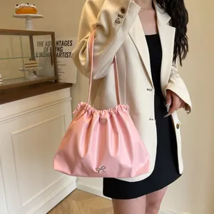 Pink pleated drawstring tote bag with silver metal bow worn by model in cafe setting